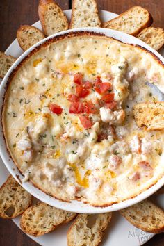 a white bowl filled with cheese and tomato dip surrounded by crackers on a wooden table