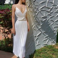 a woman standing next to a wall wearing a white dress