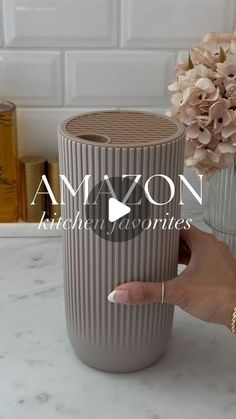 a person holding a cup in front of a vase with flowers on the counter top