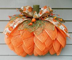 an orange mesh pumpkin hanging from the side of a house with leaves and flowers on it