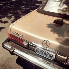 an old mercedes benz parked on the side of the road in front of a tree