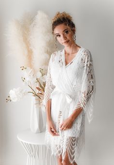 a woman standing in front of a white vase with flowers and feathers on it's side