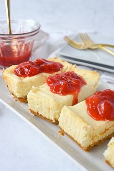 four pieces of cheesecake with strawberry toppings on a plate next to silverware