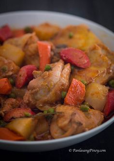 a white bowl filled with chicken, potatoes and carrots on top of a table