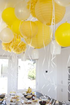 yellow and white balloons are hanging from the ceiling above a table filled with desserts