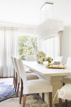 a dining room table with white chairs and flowers