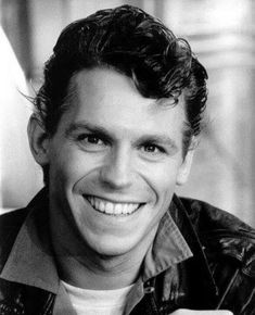 a black and white photo of a man smiling for the camera with his hand on his chest