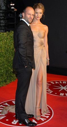 a man and woman in formal wear standing on a red carpet with their arms around each other