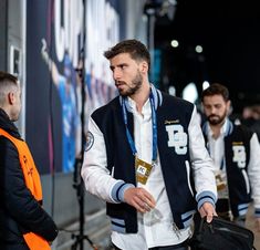 two men are walking down the street with their backpacks on and one man is wearing a vest