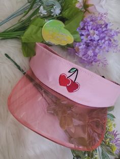 a pink hat with cherries on it sitting next to flowers