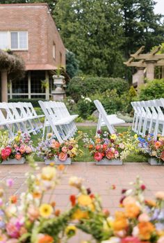 rows of white folding chairs with colorful flowers on them in front of a brick building