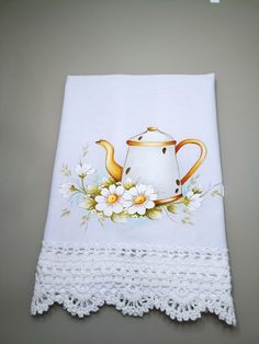 a white tea pot with flowers on it sitting on top of a doily next to a wall