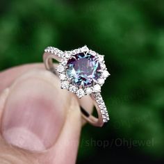 a person holding up a ring with a purple stone in the center and white diamonds around it