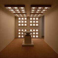 an empty room with lights on the ceiling and a vase in the center surrounded by white cubes