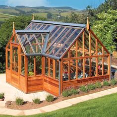 a small wooden greenhouse in the middle of a yard with lots of grass and flowers