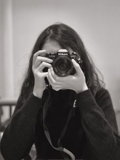 black and white photograph of a woman holding up a camera to her face with both hands