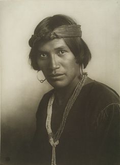 an old black and white photo of a native american woman with earrings on her head