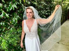 a woman wearing a wedding dress and veil standing in front of a green wall with trees