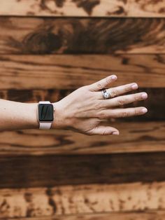 a person's hand with a ring on it and a wooden wall in the background