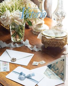 some cards and flowers on a table in front of a vase filled with white roses