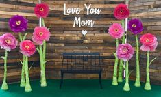 paper flowers are arranged in front of a wooden wall with love you mom written on it