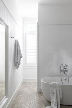 a white bathroom with herringbone tile flooring and an old fashioned claw foot tub