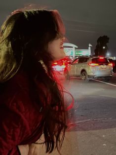 a woman standing on the side of a road at night with traffic in the background