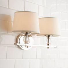 two lamps mounted on the side of a white tiled wall next to a light fixture