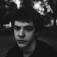 a black and white photo of a young man in a park with trees behind him