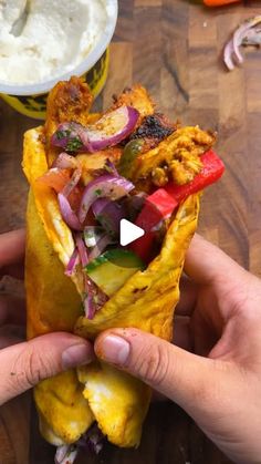 a person holding up a burrito filled with meat and veggies