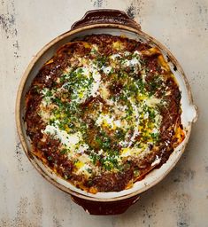 an overhead view of a baked dish with cheese and herbs on top, sitting on a table