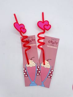 two valentine's day candy sticks with hearts attached to them on a white surface