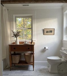 a white toilet sitting next to a wooden table with baskets on it's sides