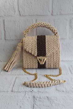 a white purse with a brown and tan stripe on the front, sitting against a brick wall