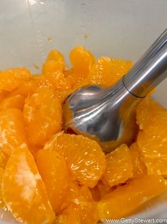 oranges in a white bowl with a metal spoon