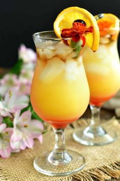 two glasses filled with lemonade and garnish on top of a table next to flowers