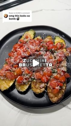 a black plate topped with slices of zucchini covered in tomatoes and parmesan cheese