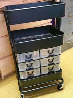 a black cart with plastic containers on it and drawers in the back ground next to cabinets