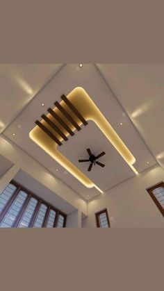 a ceiling with lights and a fan in the middle is lit by two large windows