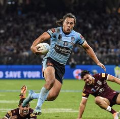 a rugby player running with the ball in his hand and two other players behind him