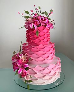 a three tiered cake decorated with pink flowers and greenery on a glass platter