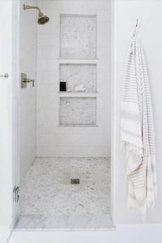 a white bathroom with marble flooring and shelves on the wall, along with a towel rack