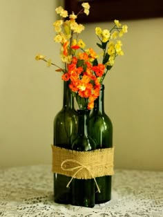 two green bottles with flowers in them on a table