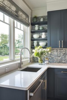 a kitchen with dark blue cabinets and white counter tops is pictured in this image, there are vases on the window sill