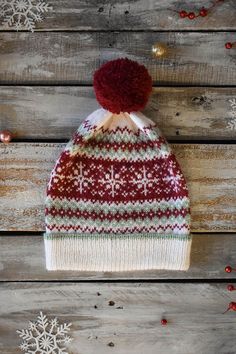 a red and white knitted hat sitting on top of a wooden table next to snowflakes