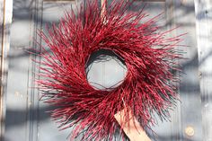 a close up of a red wreath on a door with a hand holding it in the air