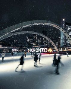 people skating on an ice rink at night in toronto, canada with the city lights lit up behind them