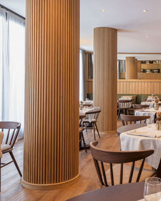 an empty restaurant with wooden columns and white tablecloths on the dining room tables