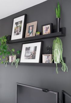 two black floating shelves with pictures and plants on them in front of a flat screen tv