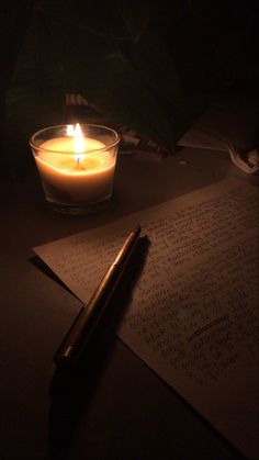 a lit candle sitting on top of a table next to a pen and paper with writing